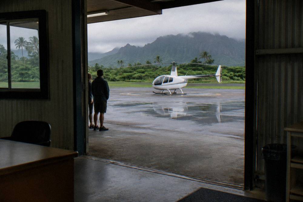A helicopter parked on a pad near a check-in office with passengers waiting