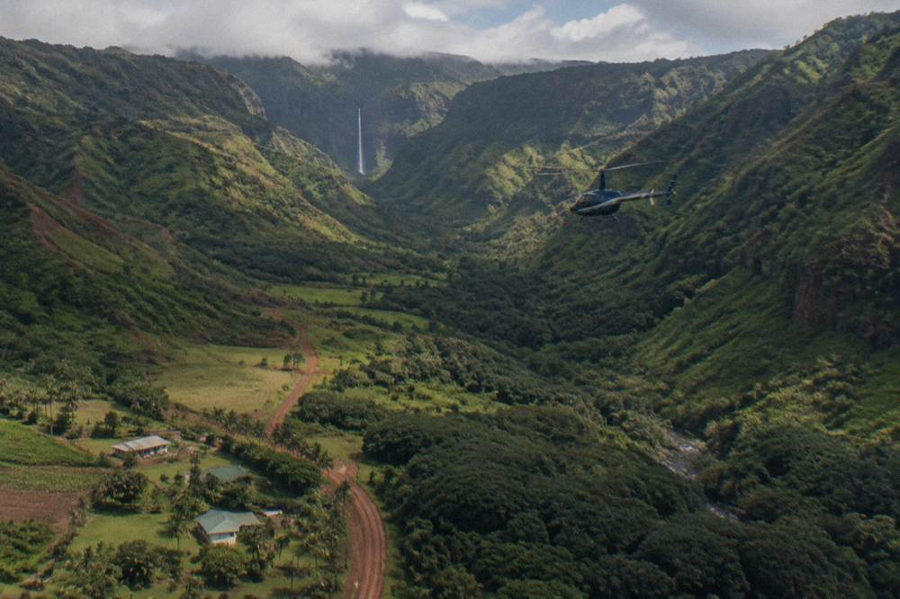 A helicopter flying above a green canyon with a waterfall in the distance