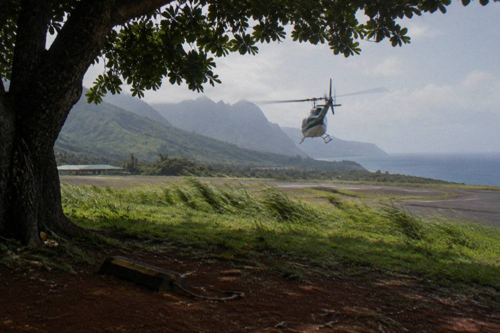 A helicopter flying over green Kauai ridges toward the sea