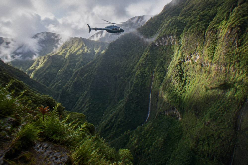 A tour helicopter cruising above deep green valley walls on Kauai