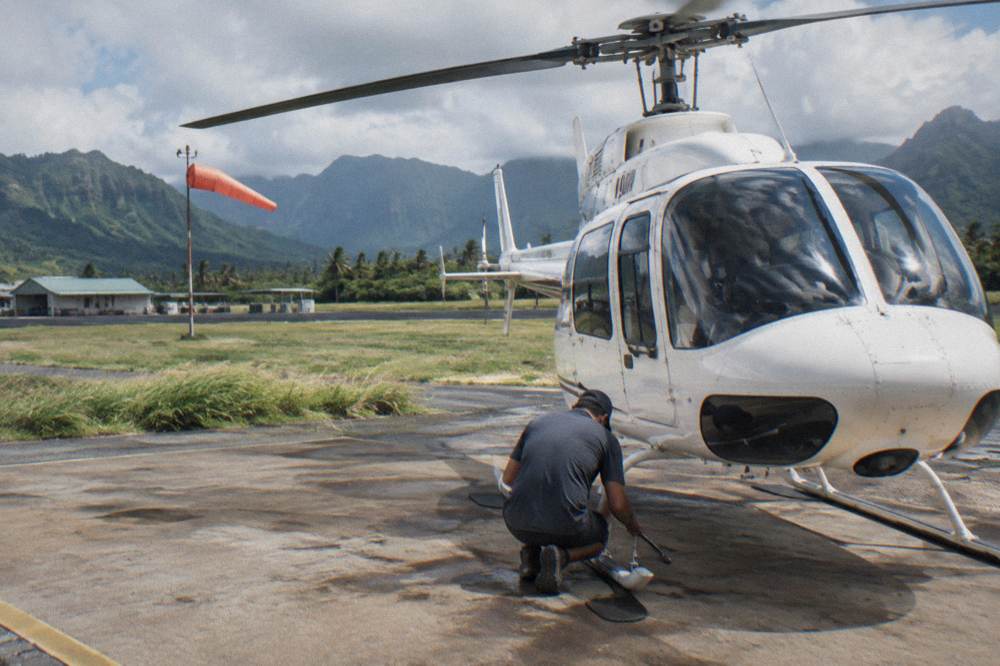 A helicopter parked on a heliport apron with crew performing a pre-flight check