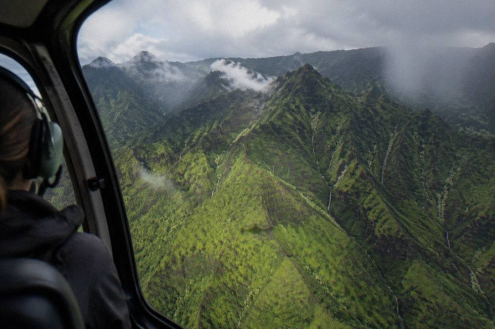 A deep green canyon with layered ridges seen from a helicopter window
