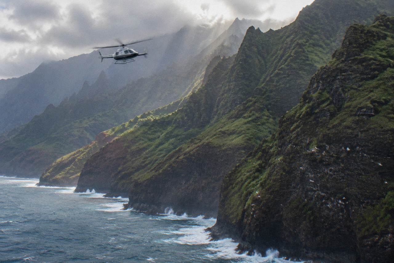 A helicopter flying along green sea cliffs above the ocean near Kauai