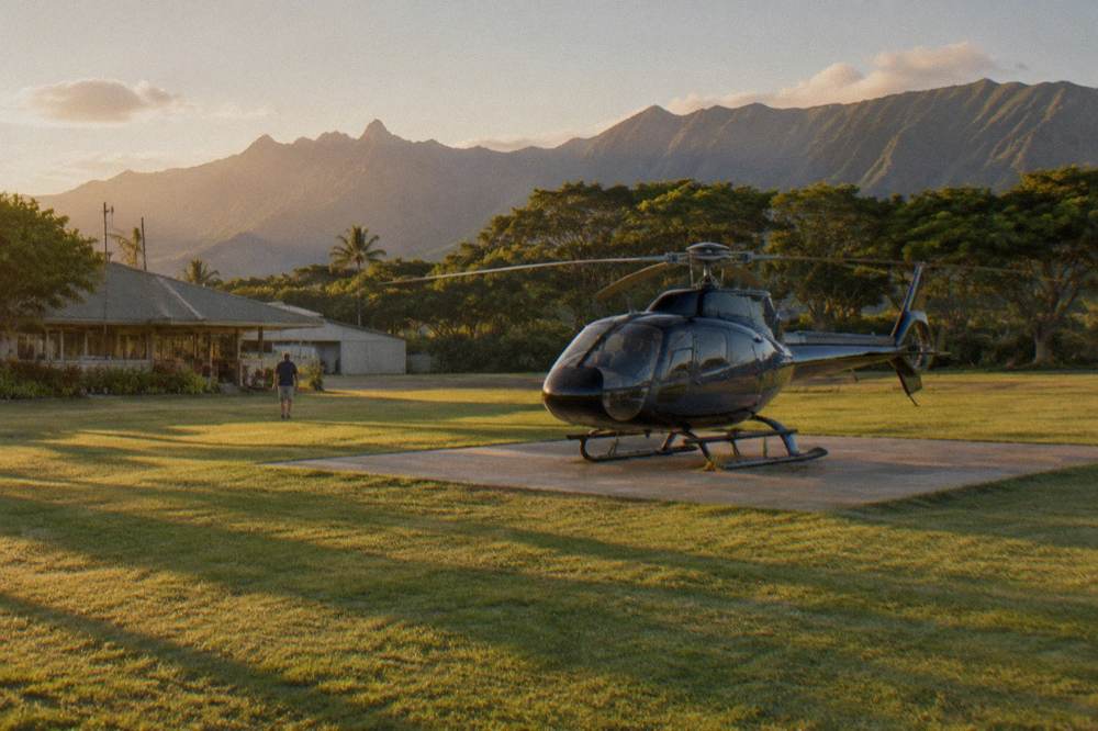 A helicopter parked on a helipad with the Na Pali Coast in the distance, late afternoon light