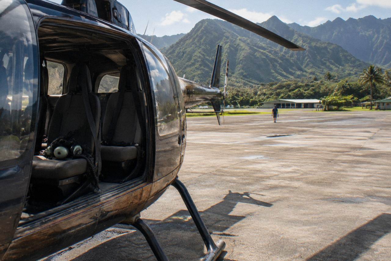 A helicopter with open doors on a sunny tarmac, green mountains in the background