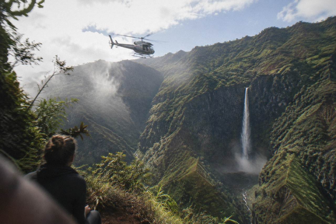 A helicopter flying above deep green Kauai valleys with a thin waterfall on the canyon wall