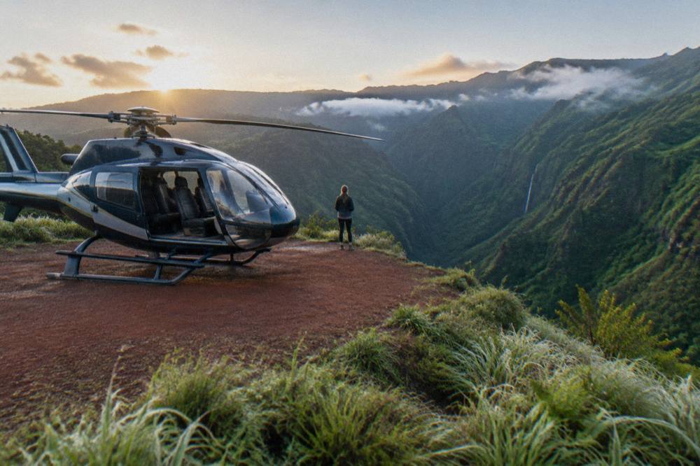 A helicopter parked on a grassy canyon rim with deep green gorge walls in the background