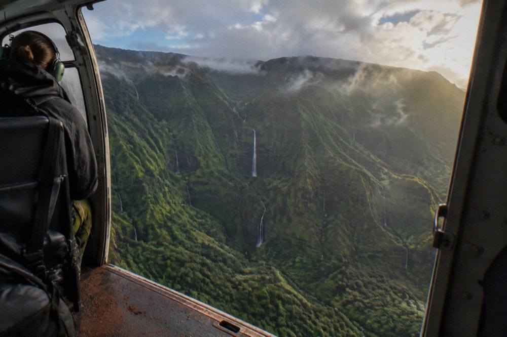 Open helicopter cabin door frame above a deep green valley with waterfalls
