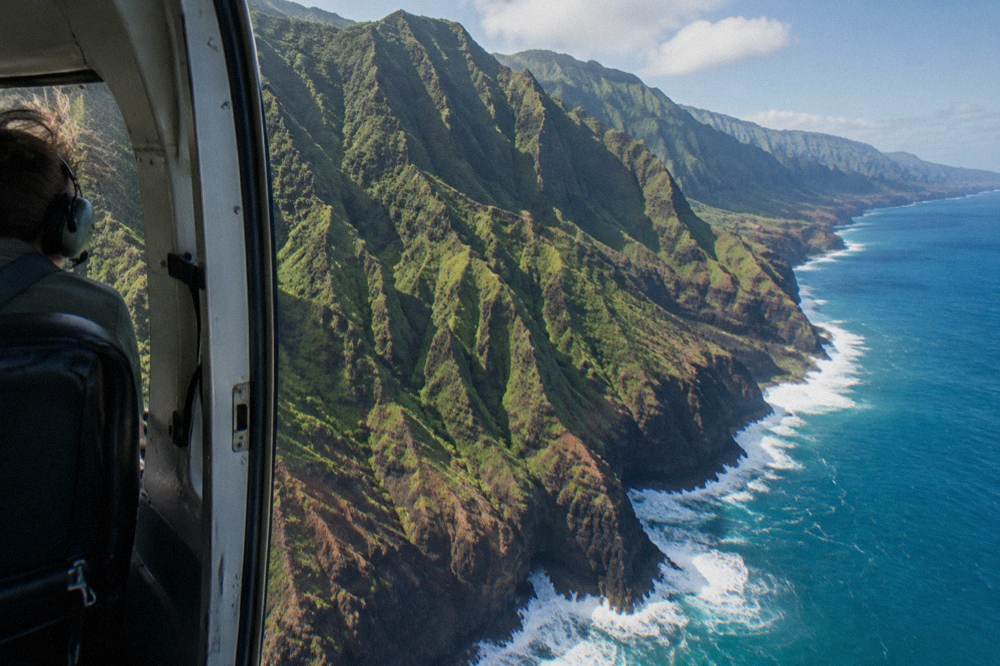 Helicopter flying along a jagged coastline with cliffs meeting the ocean