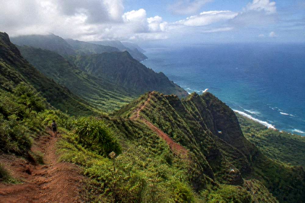 A deep green canyon with layered ridges stretching toward the ocean under scattered clouds