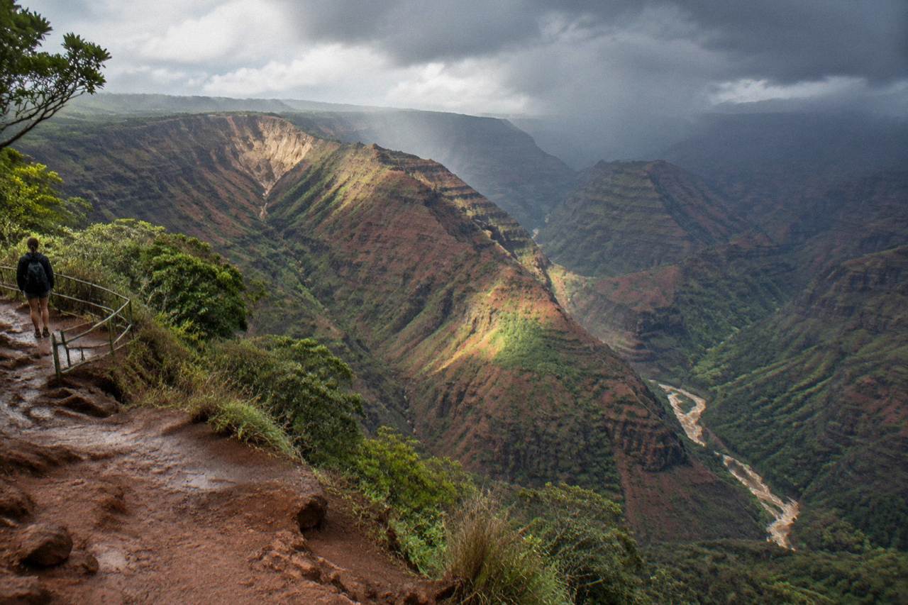 Deep eroded ridges of a red and green canyon under scattered clouds on Kauai
