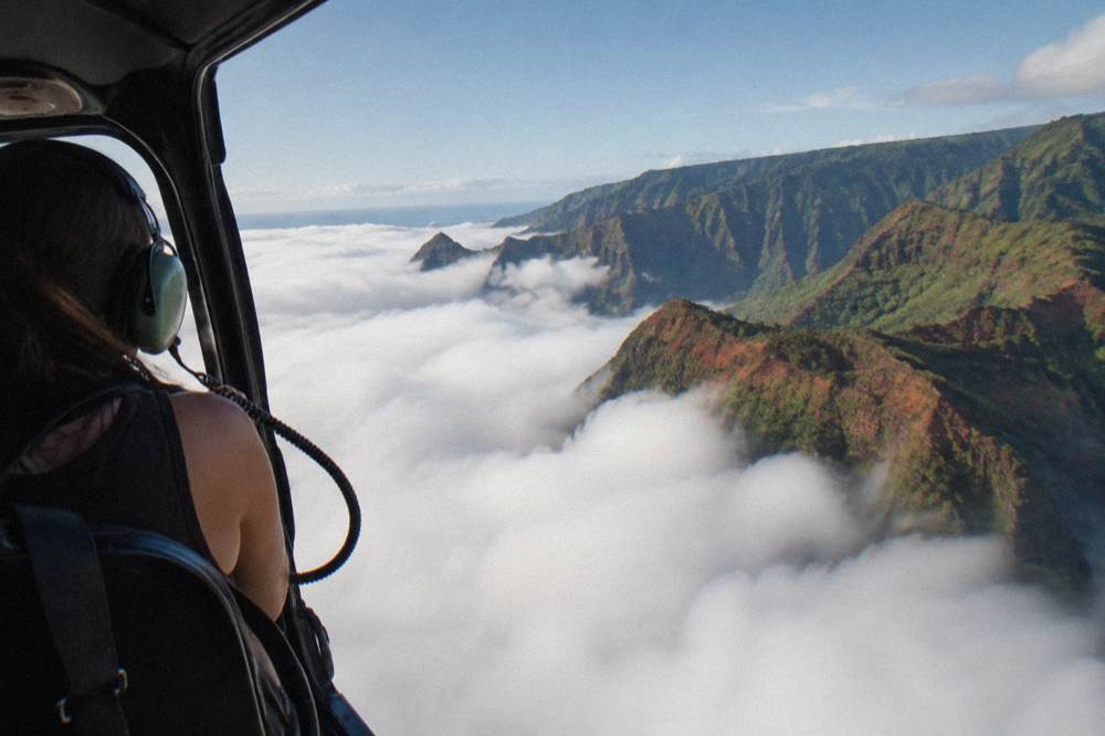 A helicopter flying above clouds along a green Kauai valley