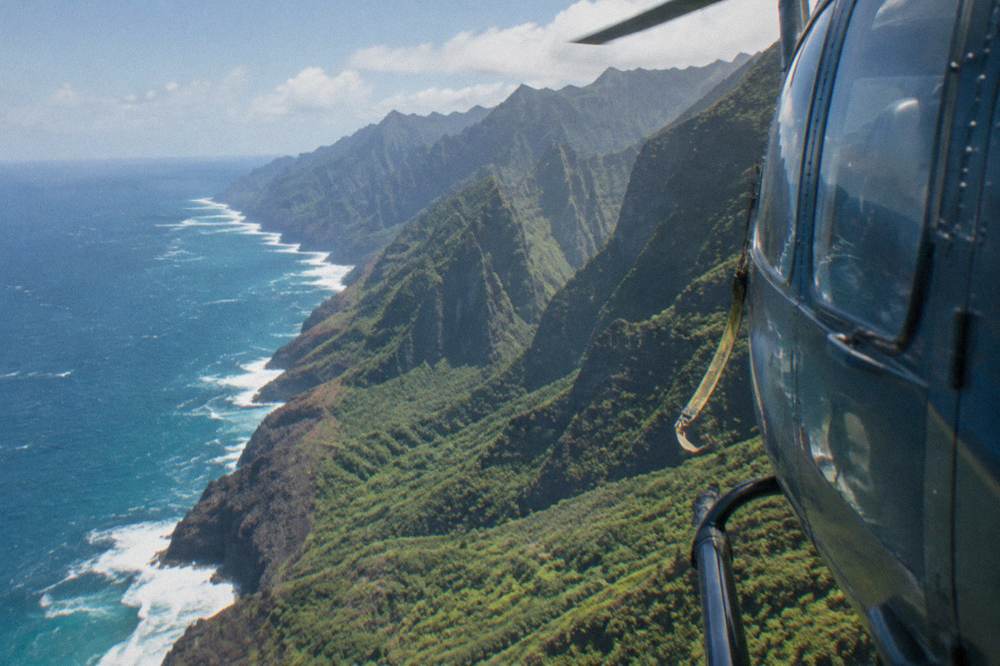 A helicopter flying along steep coastal cliffs above the ocean