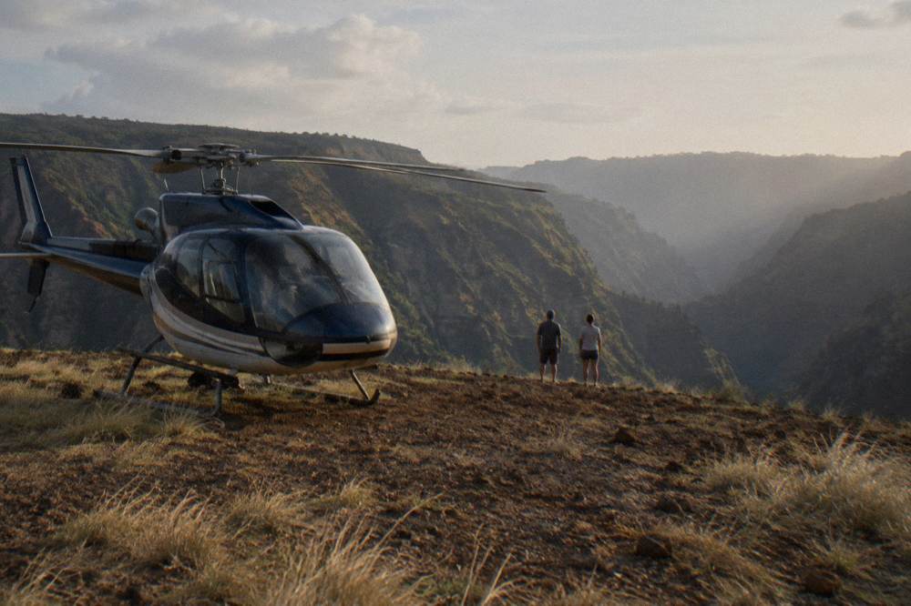 A helicopter parked on a grassy canyon rim with valley walls rising behind it