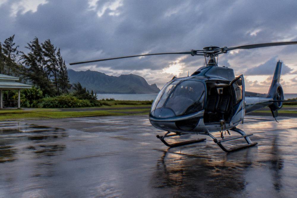 A small tour helicopter on a paved heliport pad near the coast