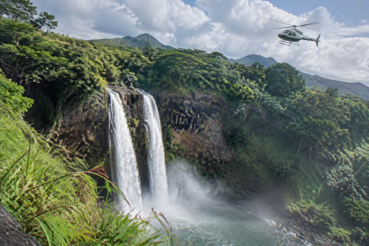 A helicopter flying over deep green Kauai canyons and waterfalls
