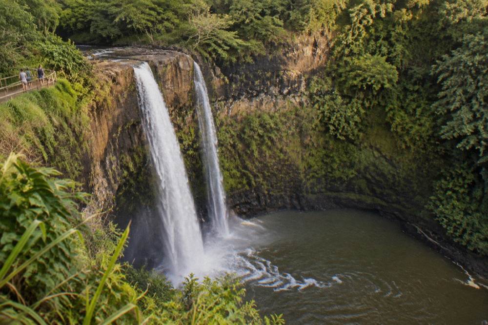 A waterfall dropping into a green Kauai valley seen from above