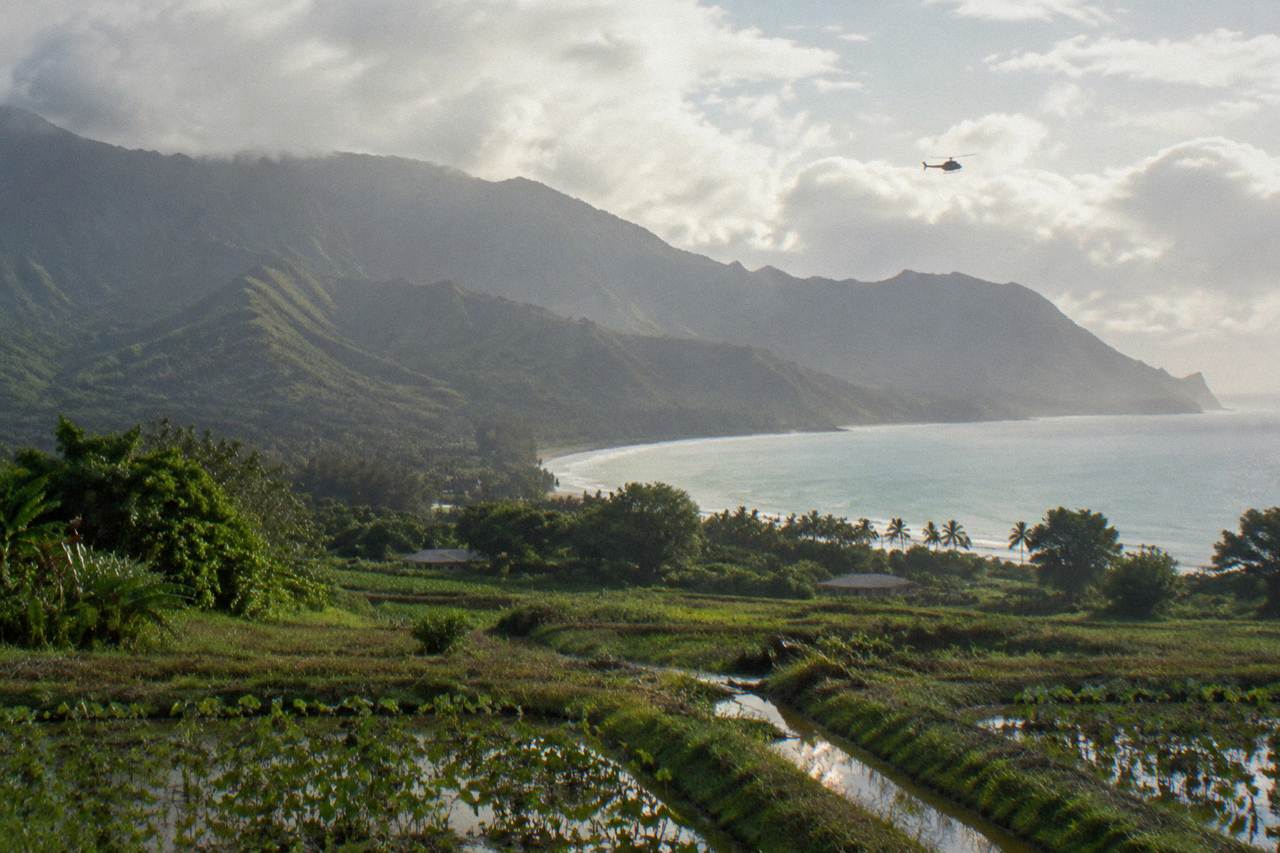 A helicopter flying above green Kauai valleys under soft morning light