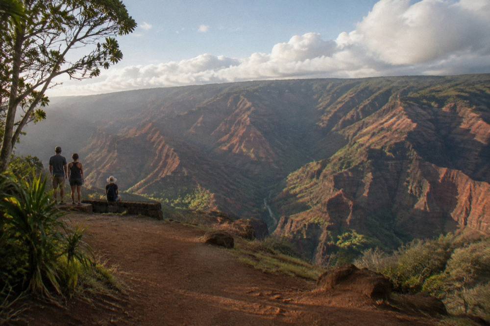 A wide canyon with red and green walls under a partly cloudy sky