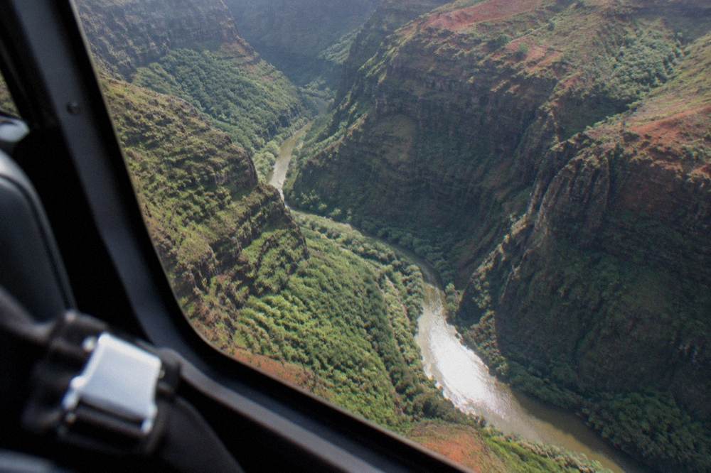 A helicopter cabin view of a deep green canyon with a river below
