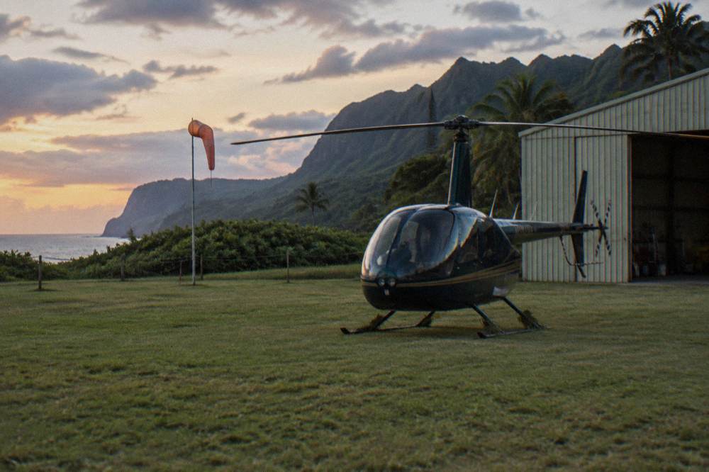 A small helicopter parked on a grass apron near a hangar