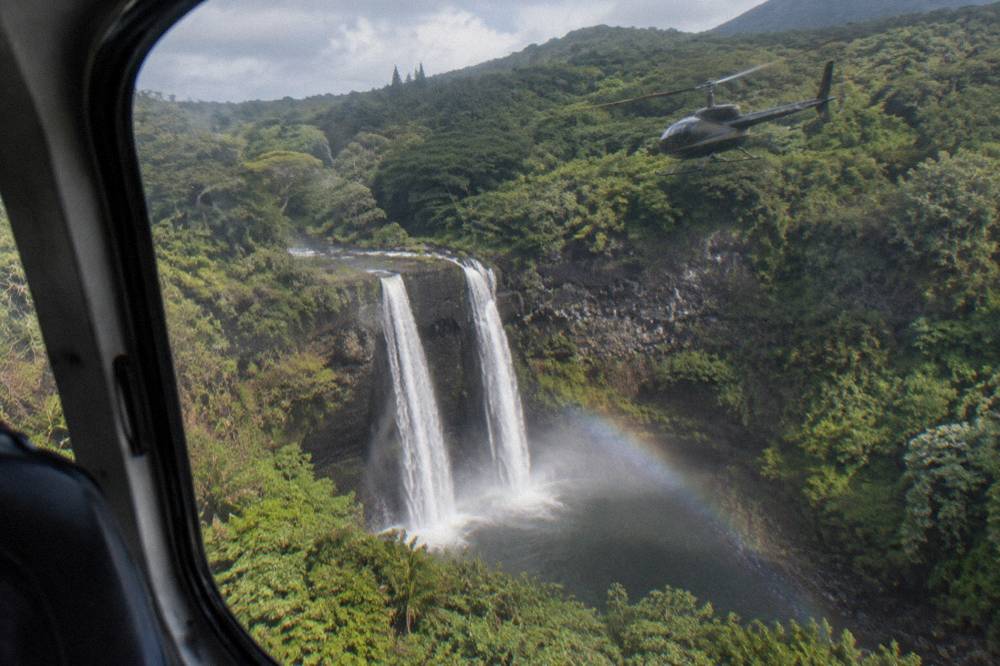 A helicopter with closed doors flying above a canyon with waterfalls