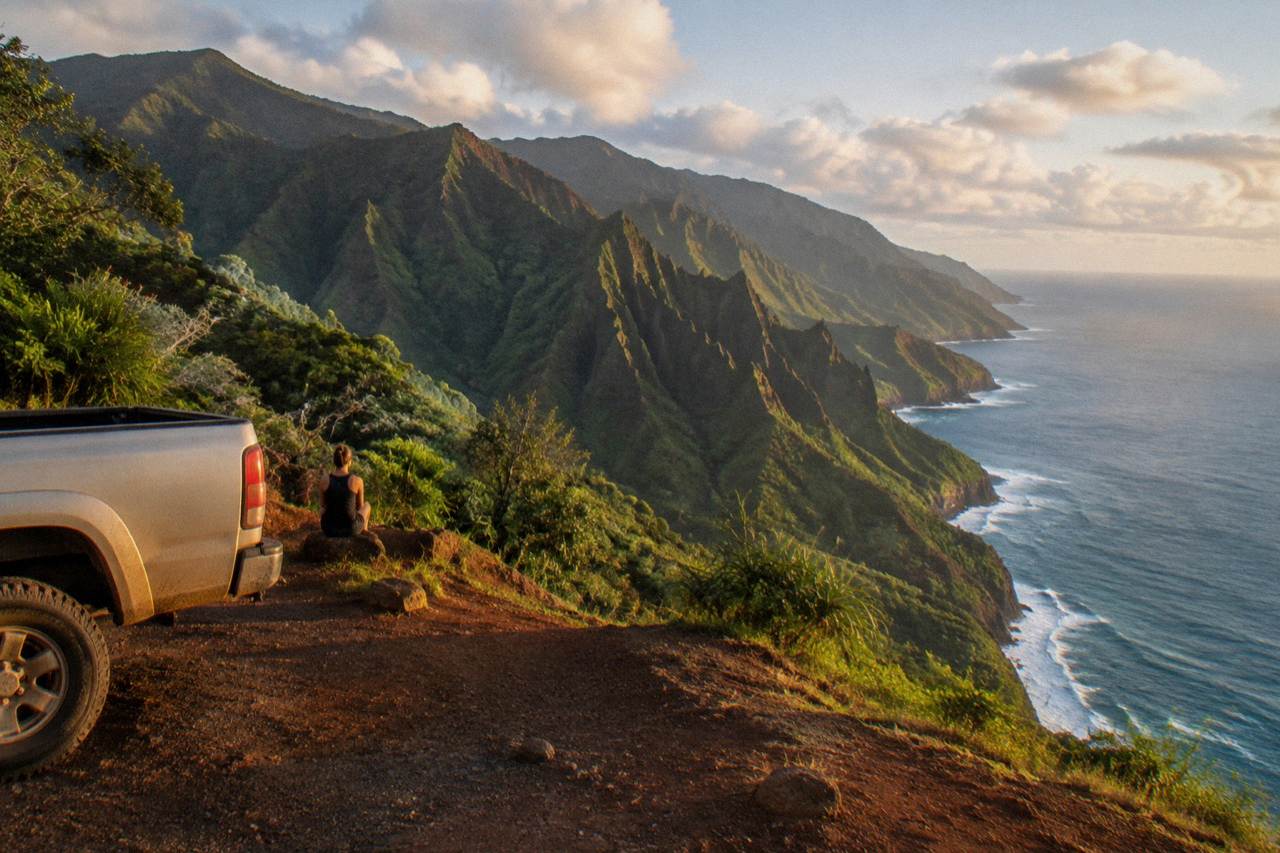 A wide coastal view of green Kauai cliffs meeting the ocean under scattered clouds