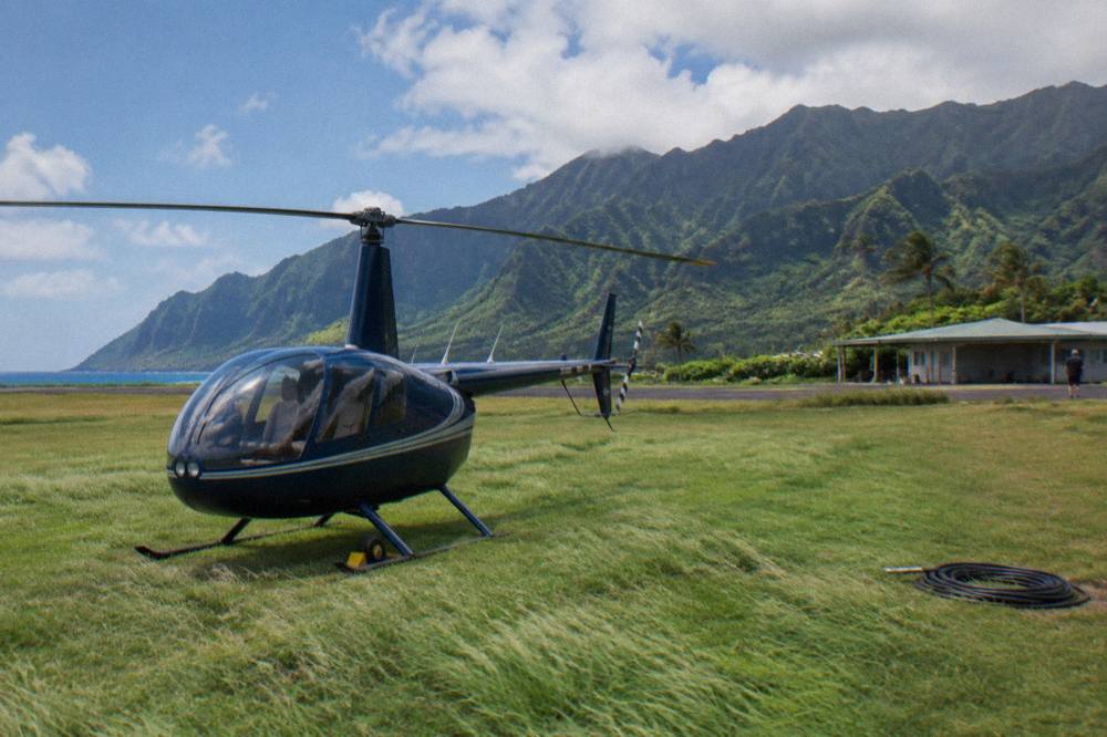 A small helicopter parked on a grass pad near green cliffs