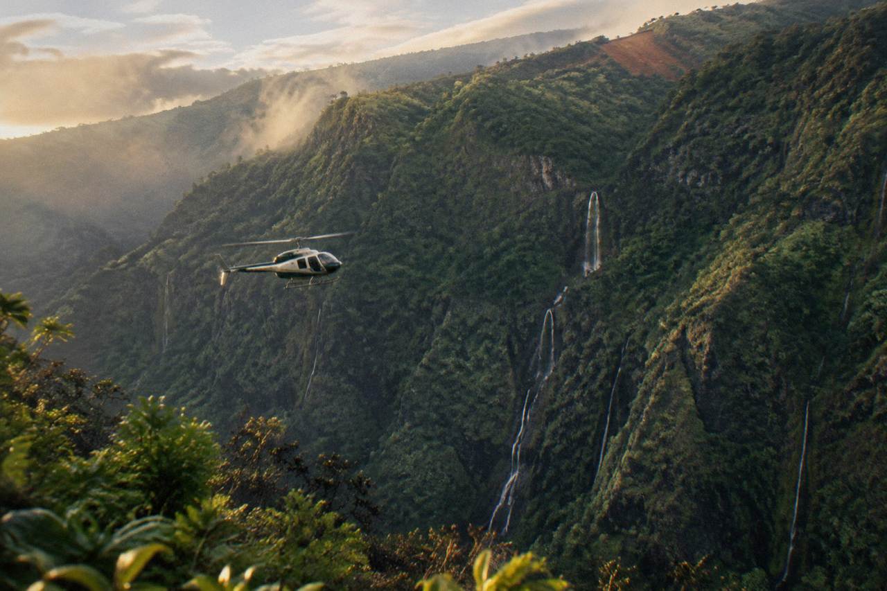 A helicopter flying over deep green Kauai canyons and waterfalls