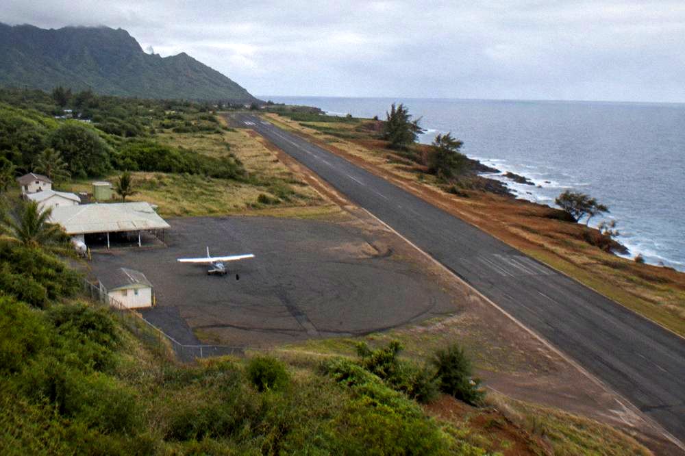 Aerial view of a runway and heliport beside a green coastline with ocean beyond