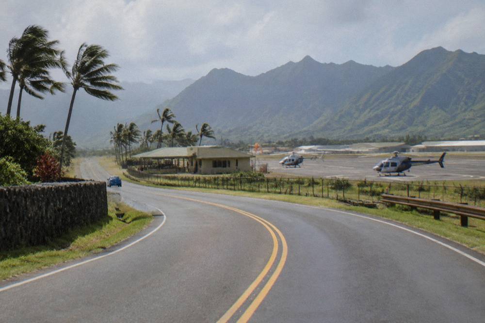 A coastal road curving toward a small airport area with palm trees and distant mountains