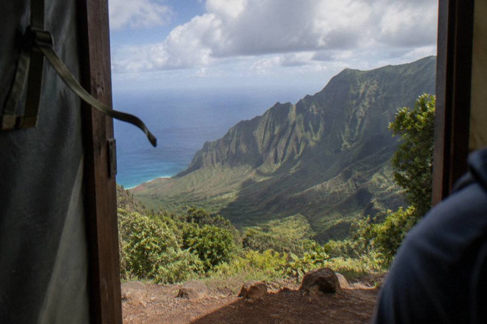 Open helicopter door frame above a deep green canyon with ocean in the distance