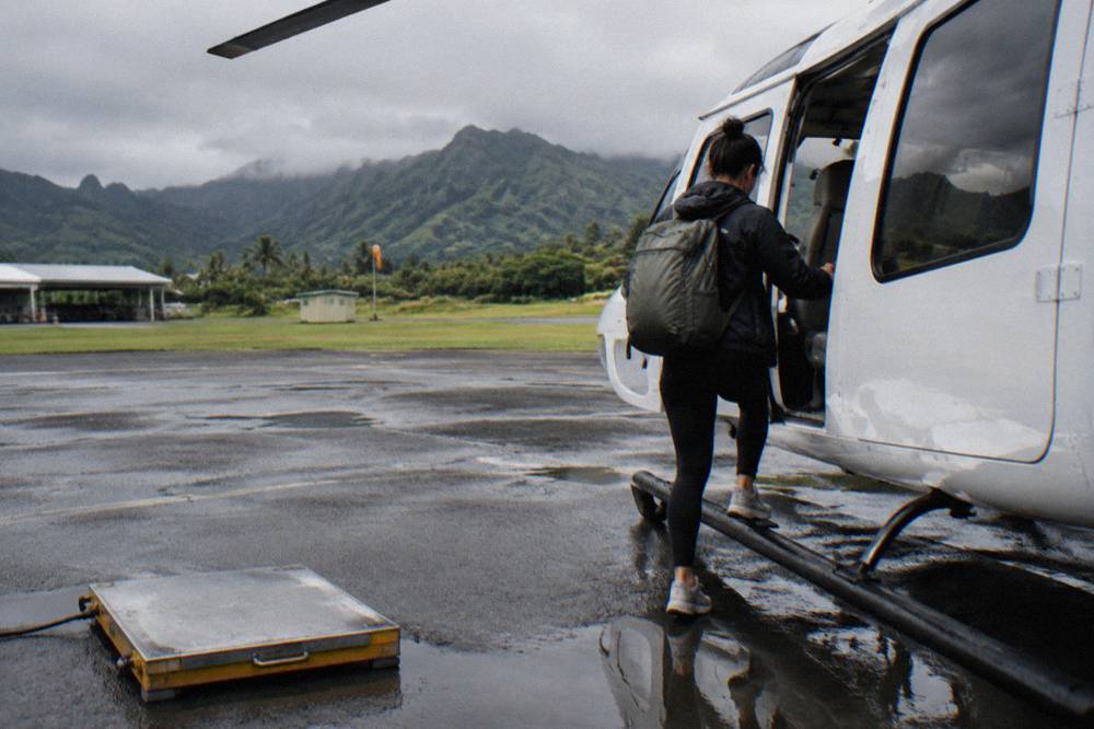 A passenger stepping onto a helicopter skid beside a check-in scale at a Lihue heliport