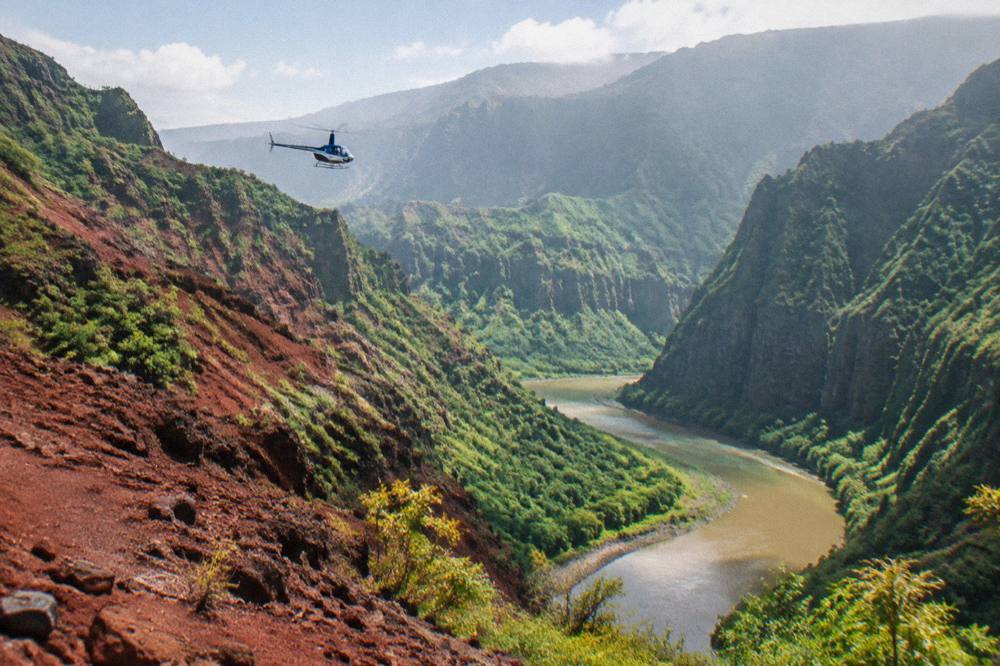 A helicopter flying above a red rock canyon with a wide river valley below