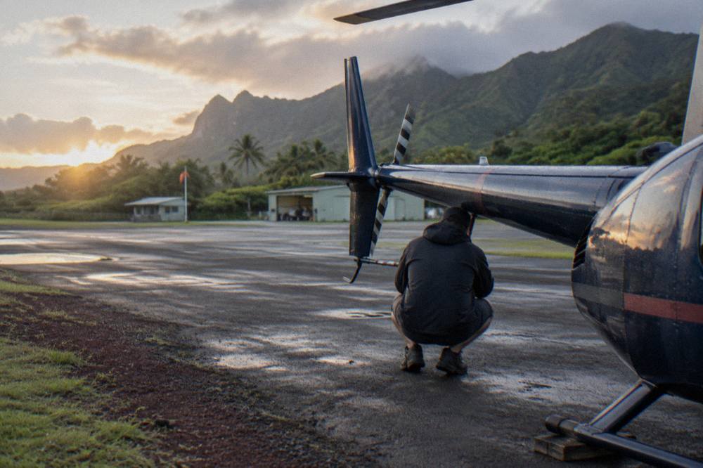 A tour helicopter parked on a heliport apron with crew performing a pre-flight walk-around