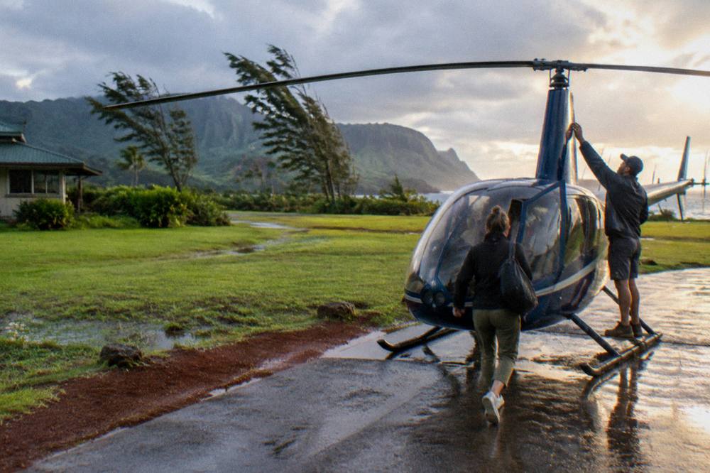 A small-group helicopter on a grass apron on Kauai with passengers boarding