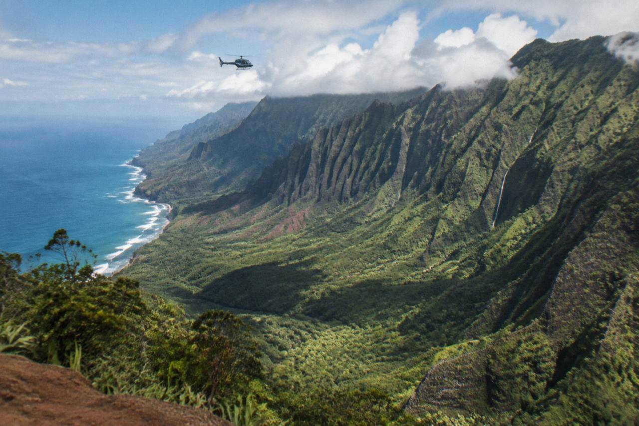 A helicopter flying above deep green Kauai valleys with clouds resting on the ridgeline
