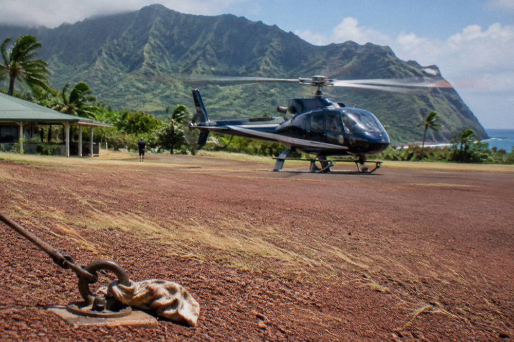 A tour helicopter parked on a heliport apron with rotor blades still turning