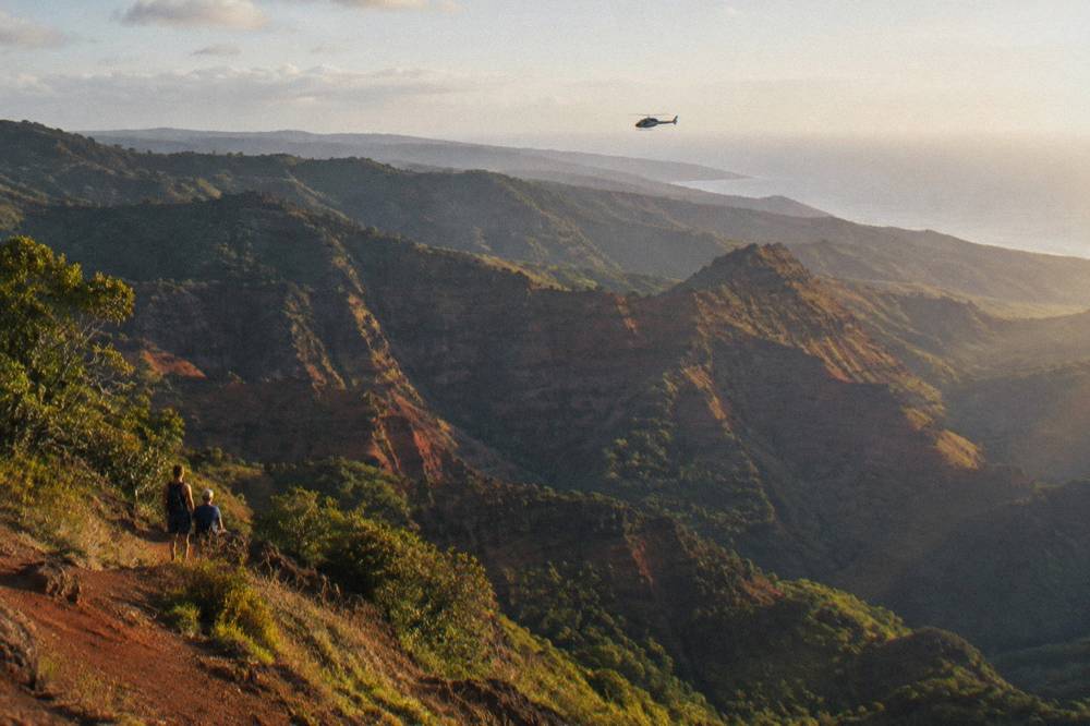 A helicopter flying above a deep green canyon with layered ridgelines