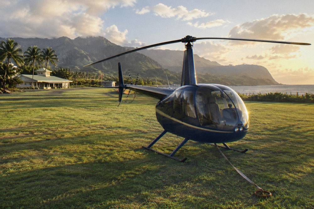 A small four-seat helicopter parked on a helipad with rotor blades still