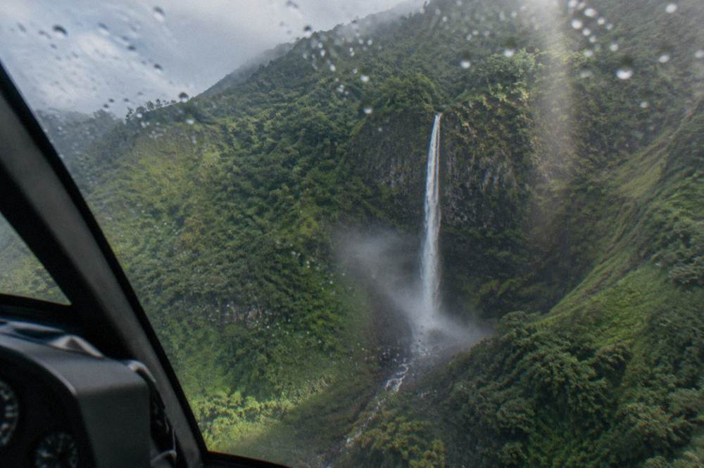 A waterfall pouring down a green cliff face inside a misty mountain crater