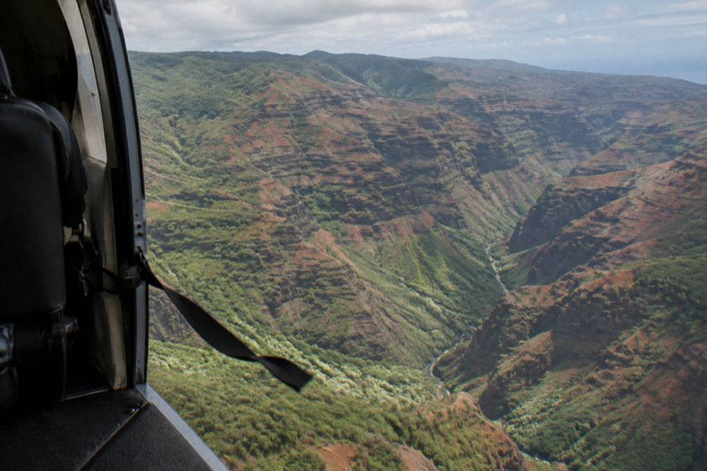 An open helicopter door frame view over a red and green canyon landscape