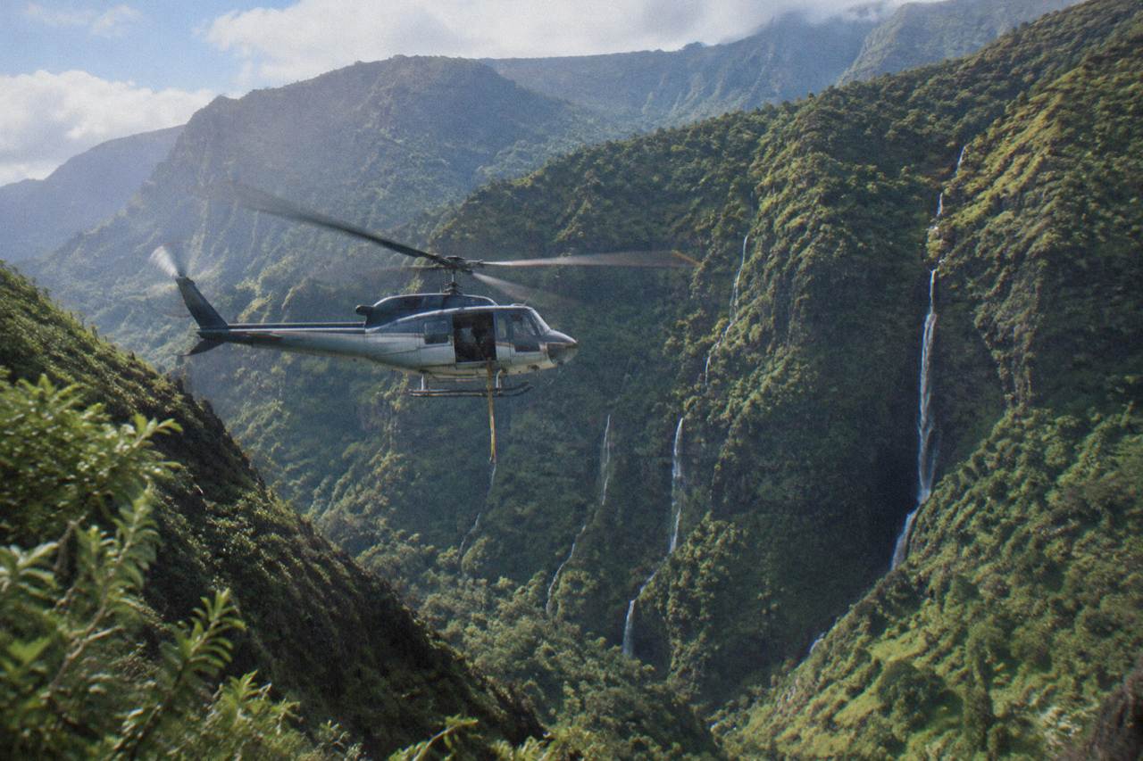 A helicopter flying over deep green Kauai canyons with waterfalls in the distance