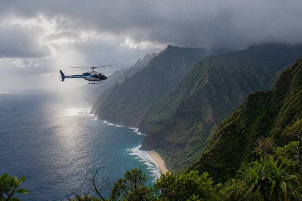 A helicopter passing over deep green ridges above the ocean