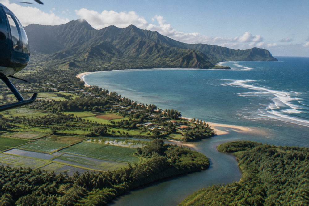 A helicopter above a curving bay with taro fields and a reef line