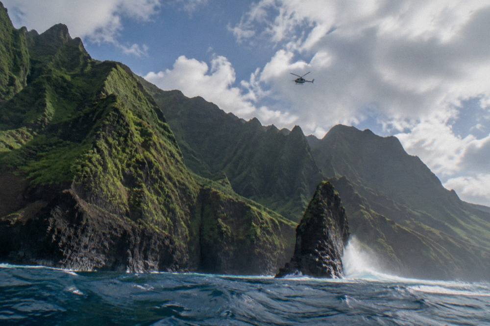 A helicopter flying above green sea cliffs along a coastline
