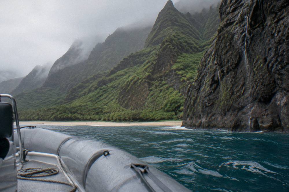 A small boat cruising near the base of tall coastal cliffs