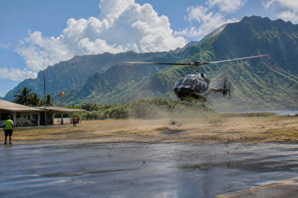 A helicopter lifting off from a heliport with green mountains in the distance