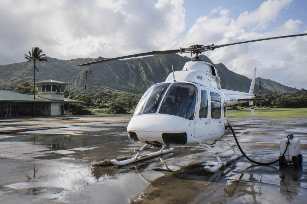 A helicopter parked on a paved heliport apron with green Kauai hills behind it
