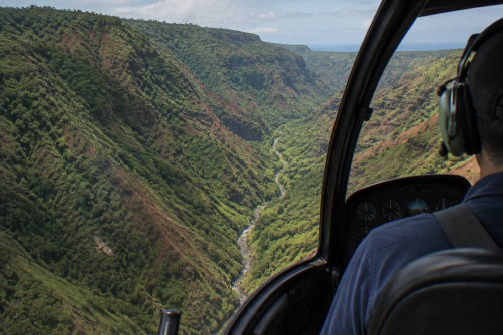 A helicopter cockpit view of a deep green canyon with a river below
